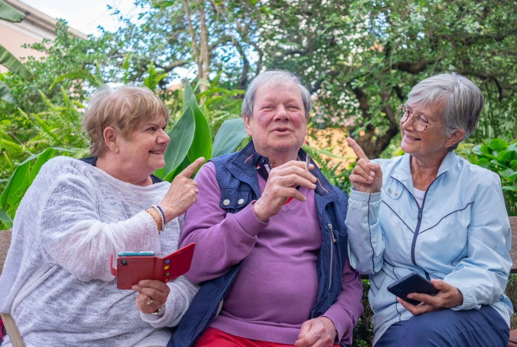 Happy group of three seniors sitting relaxed on the park bench. The man smokes a cigarette